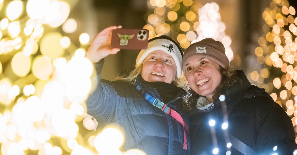 Two women taking a selfie surrounded by bright holiday lights.