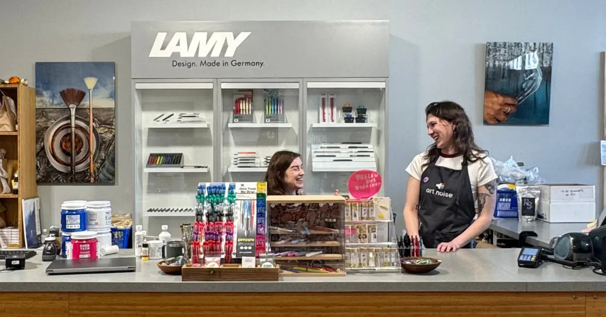 Two employees interact at the Art Noise retail store counter with various products displayed.