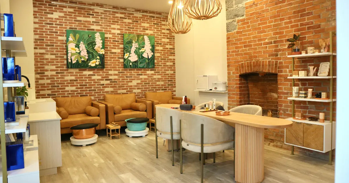 Cozy interior of La Bella Beauty Bar with brick walls, manicure and pedicure stations area, and shelves with various skin care products.