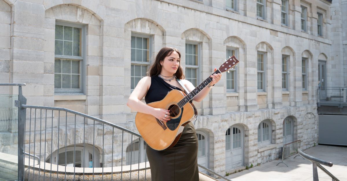 Savannah Shea playing guitar outdoors near Kingston City Hall