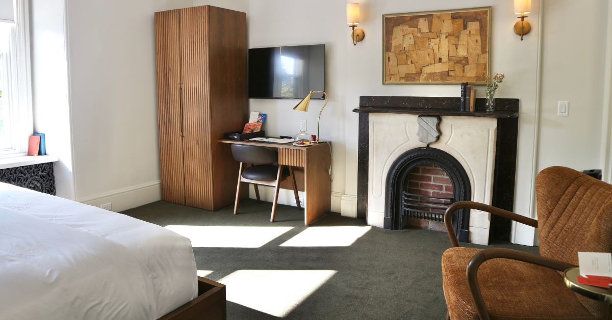 A cozy hotel room featuring a bed, desk, TV, and fireplace.