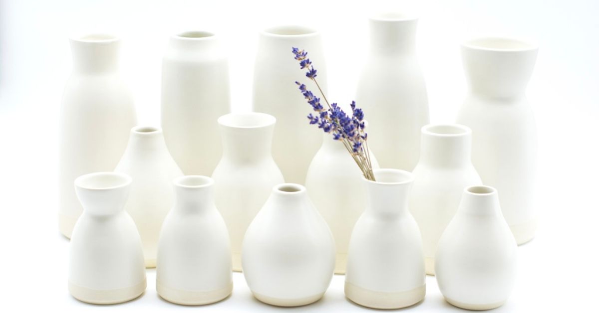 A collection of white vases with lavender flowers in one.