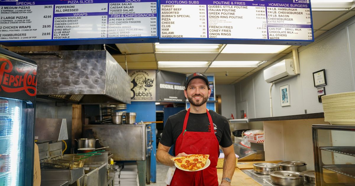 Smiling man in red apron holding food in a restaurant kitchen.