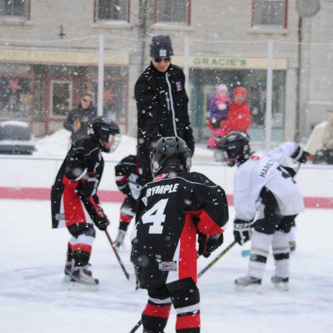 young kids in hockey gear waiting for a puck drop at an outdoor skating rink in downtown kingston.
