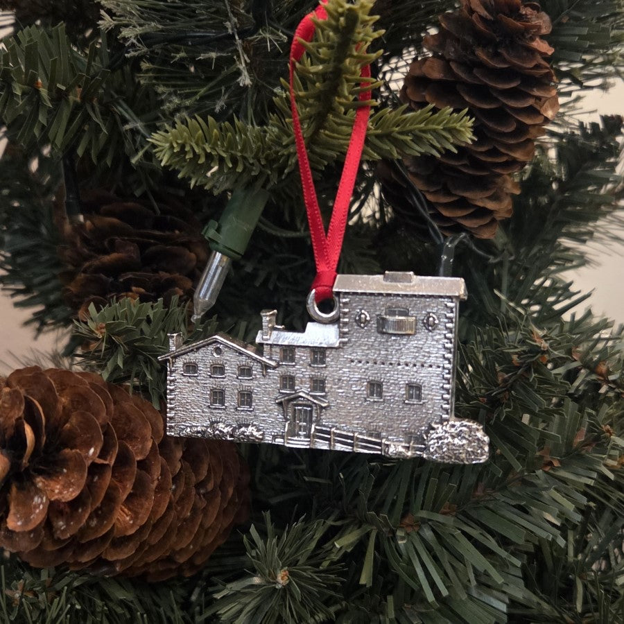 Silver building ornament on a red ribbon with pine cones and greenery