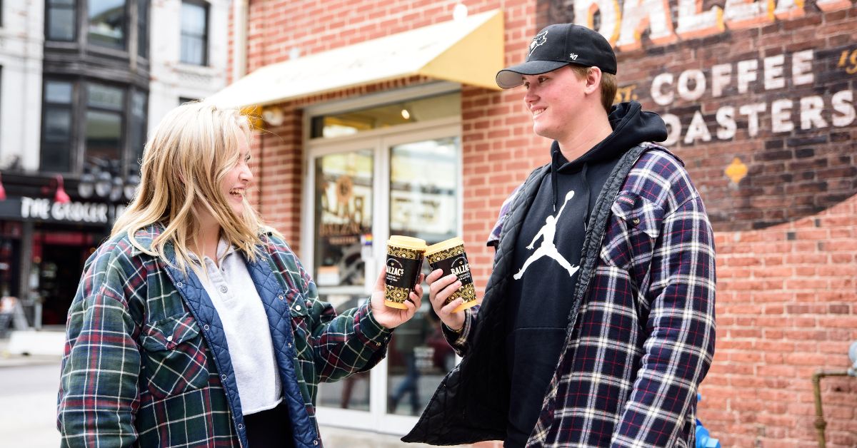 Two people holding takeaway coffee outside a downtown Kingston coffee shop.