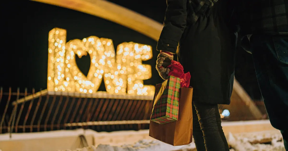 Person holding a gift in front of illuminated "love" sign at night.