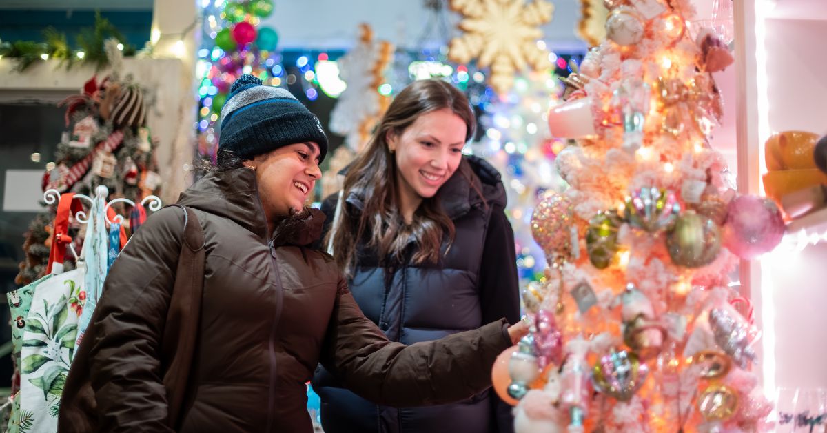 Two women admiring a decorated Christmas tree in a festive setting.