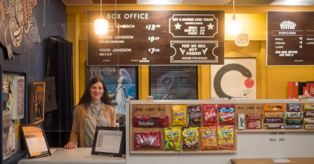 Independent movie theatre in Kingston box office with staff member, ticket prices, and candy display at The Screening Room.
