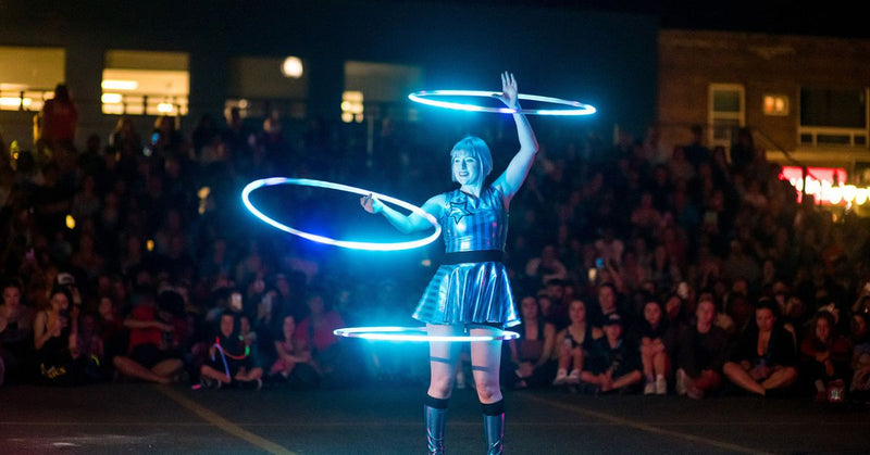 Person performing with glowing hula hoops in front of an audience at night.