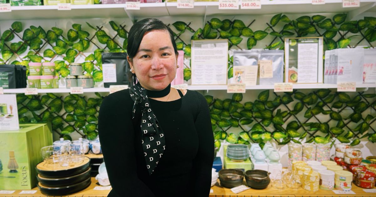 Smiling woman in front of shelves filled with products and greenery background.