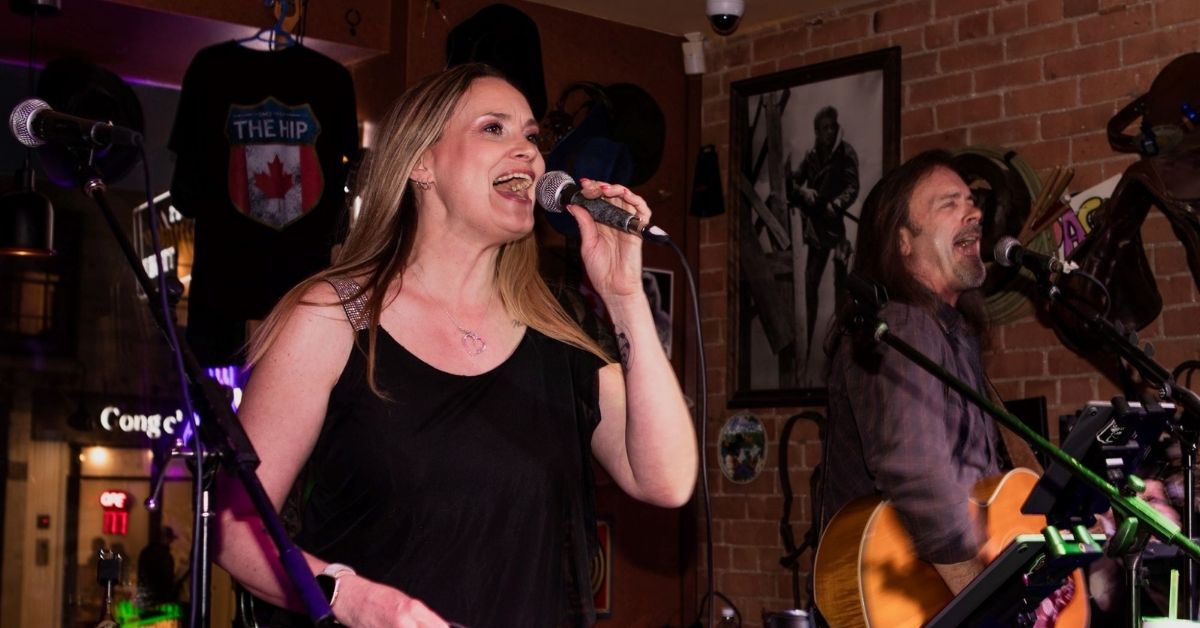 A singer performing on stage with a guitarist in the background.