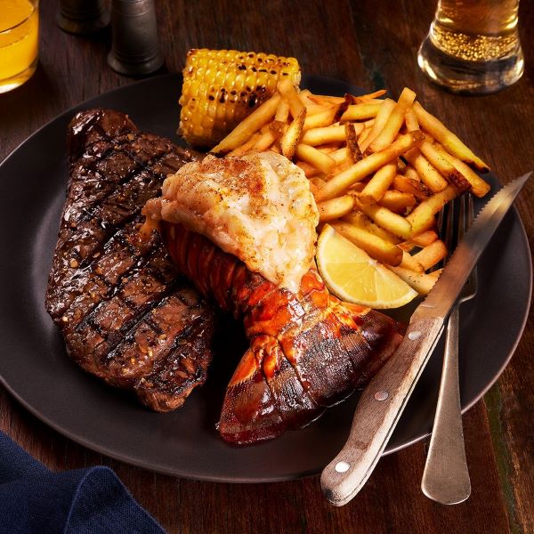 Plated meal with steak, lobster tail, fries, and corn on a wooden table at Chuck's Roadhouse