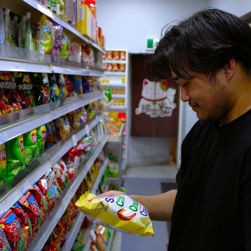 Man holding a snack package in a grocery store aisle with shelves stocked with various products.