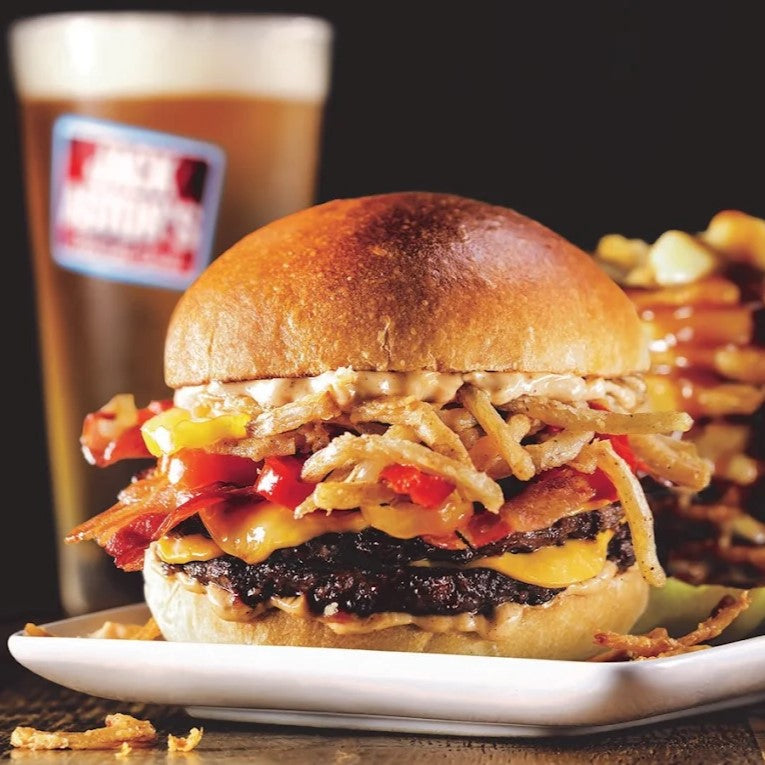 Hamburger with fries on a plate in front of a full Jack Astor's glass 