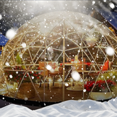 Transparent dome structure with interior decor, surrounded by snowfall
